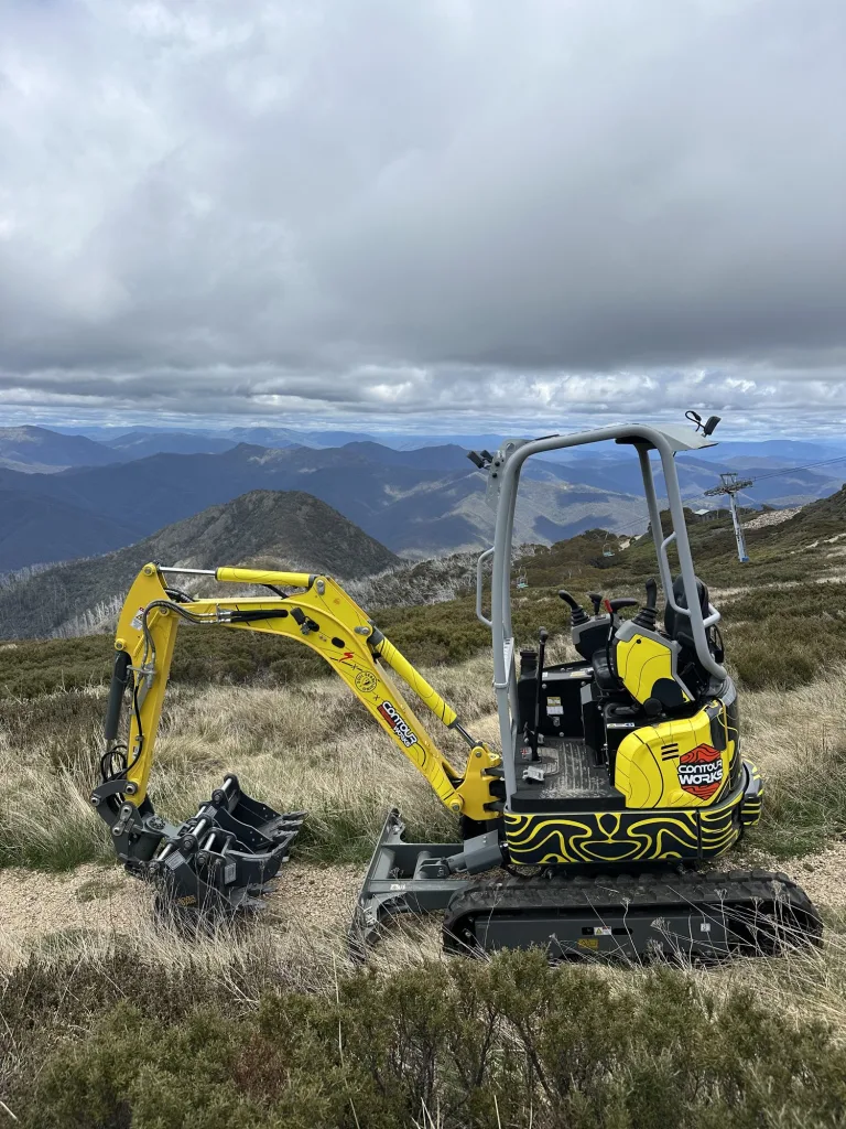 Excavator working in alpine tussock with the ranges behind